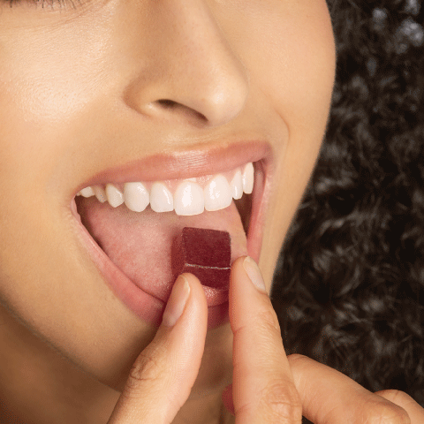 Young lady enjoying a gummy vitamin. The gummy is dark red in colour and slightly transparent to highlight the sweetness of the supplement gummy. 